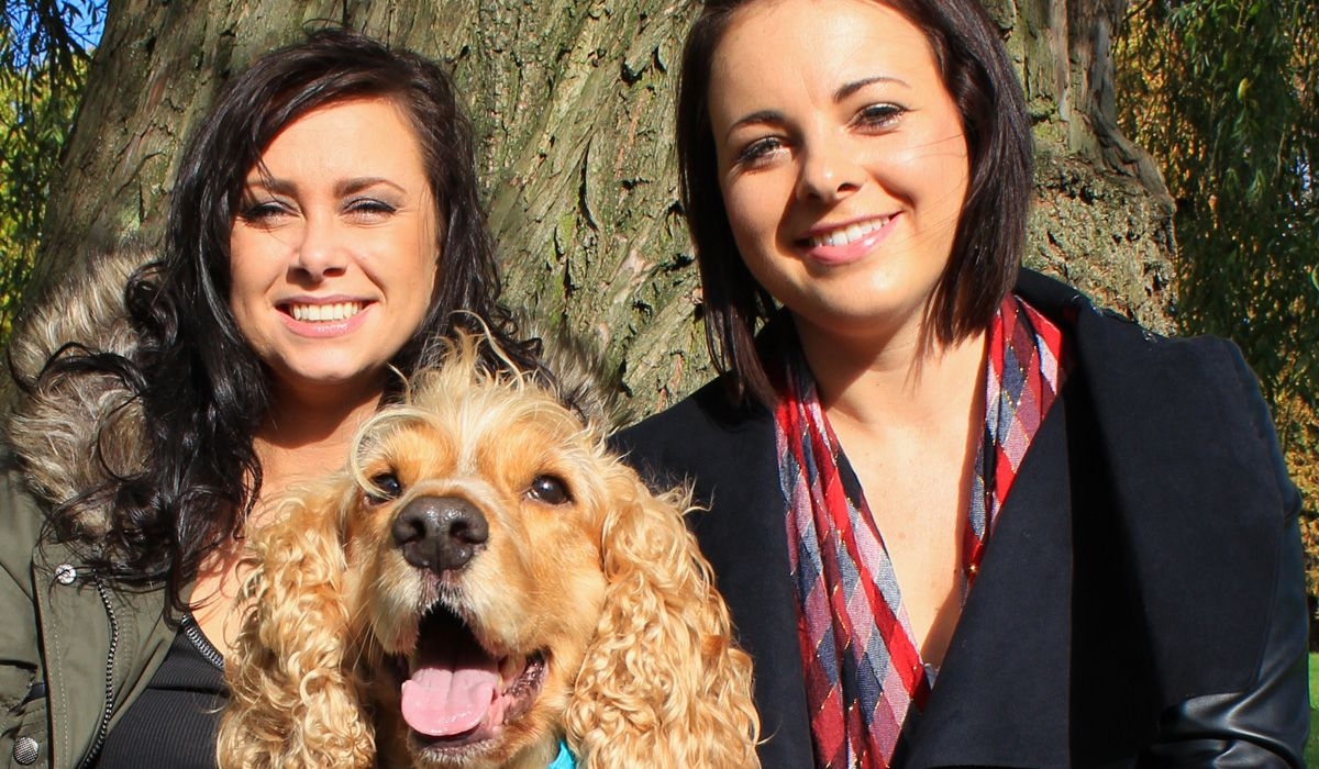 A golden spaniel looks happy posing with two smiling ladies