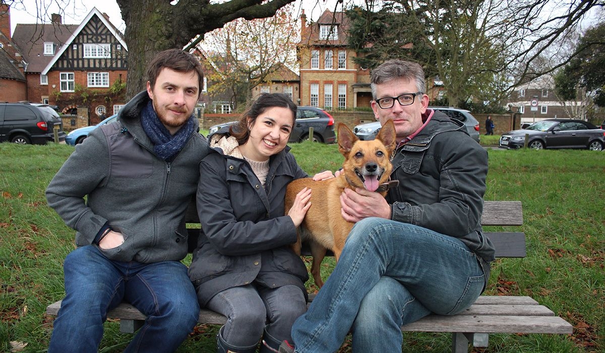 3 people on a bench in the park with a beautiful dog