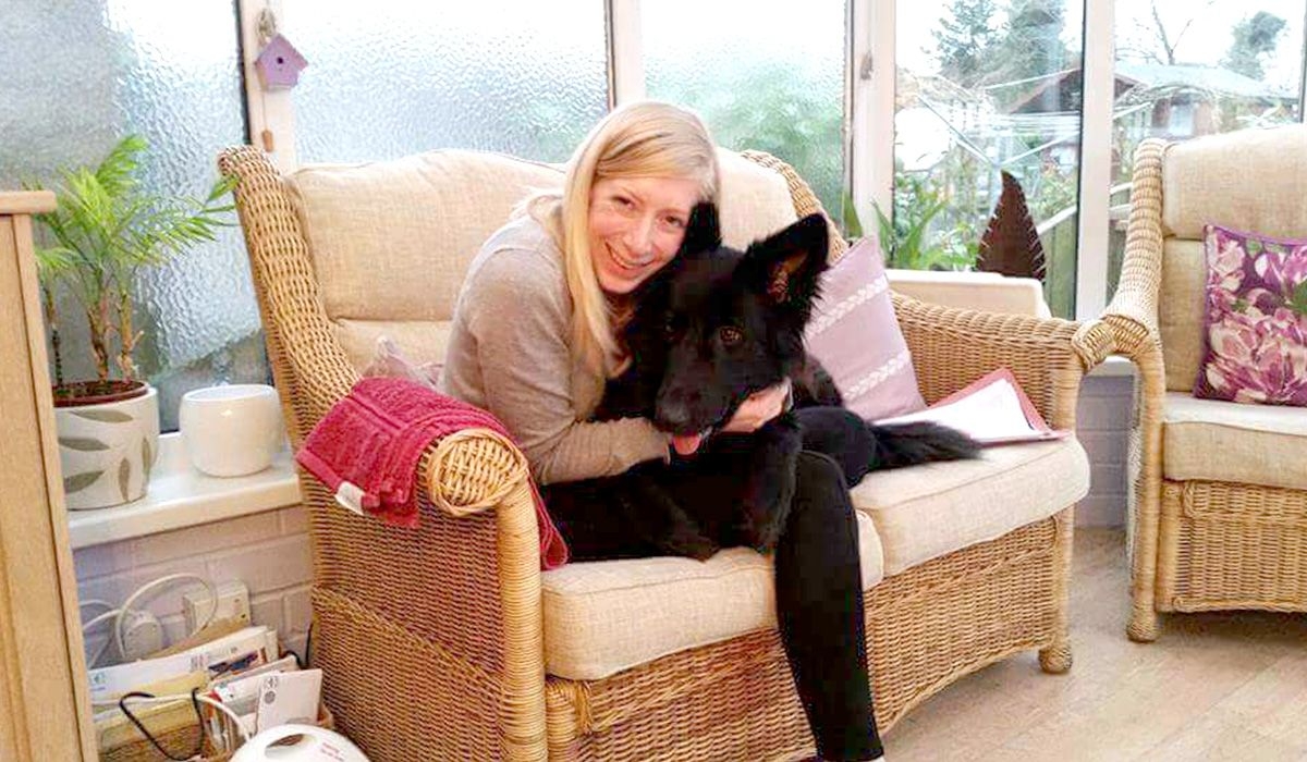 A blonde woman on a sofa cuddling a large black dog