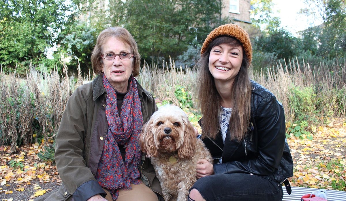 Two people are sitting on a bench together with a golden, curly-haired doggy in between them