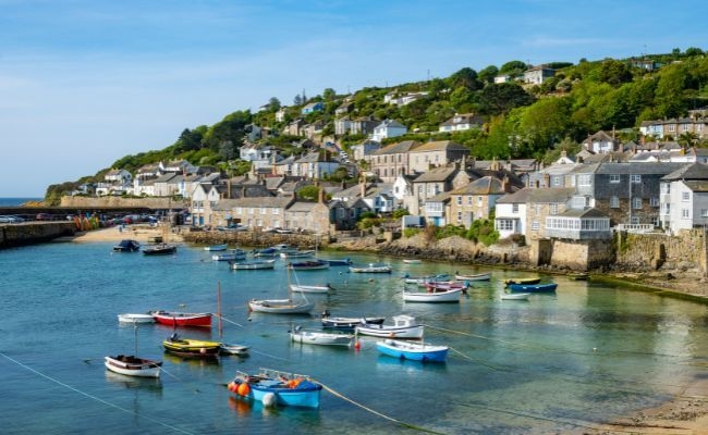 The harbour at Mousehole Fishing Village with a number of small fishing boats in an array of colours 