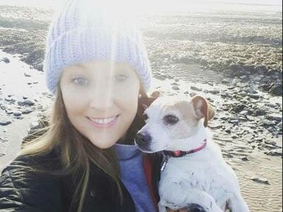 Charlotte holds a small dog while on a stoney beach