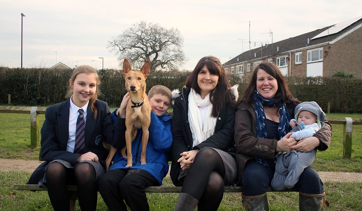 Two adults, three children and a dog are all squeezed onto a bench in a residential area.