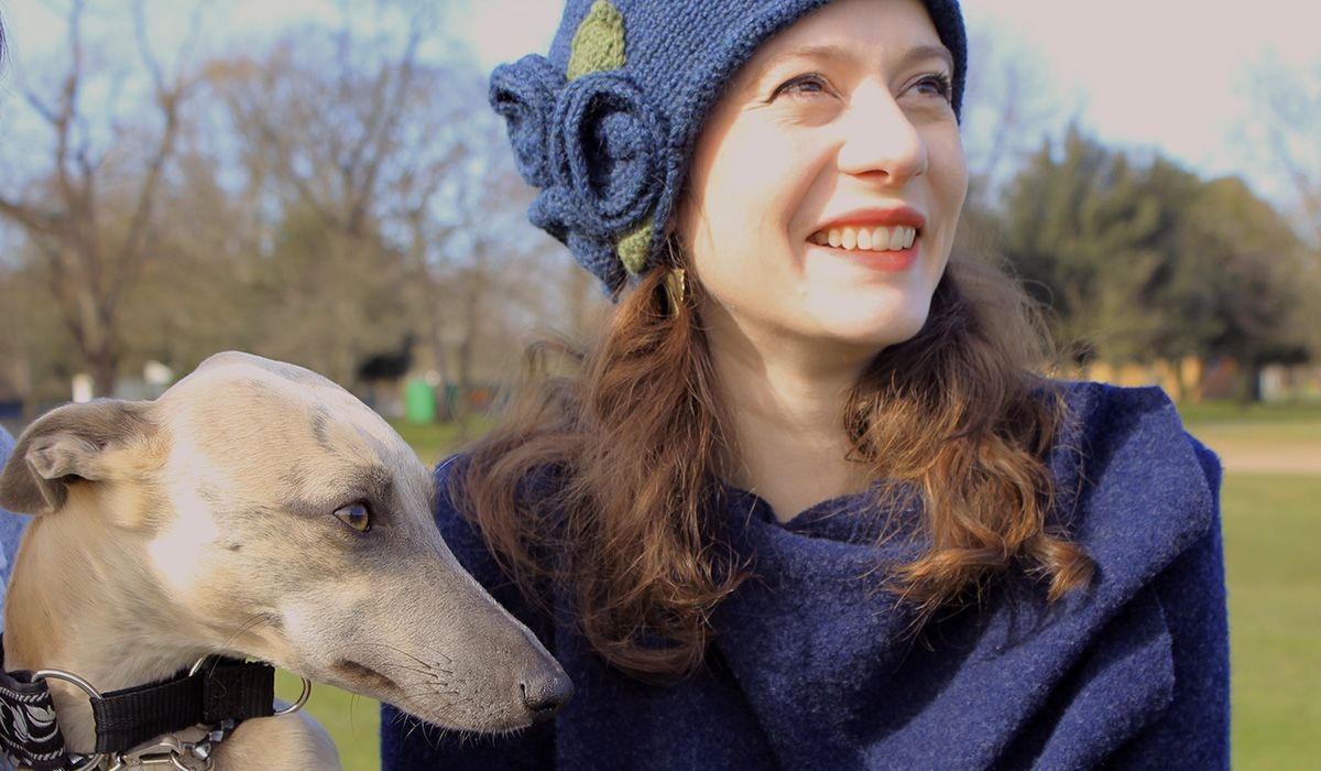 Minnie the Whippet stares off into the distance, sitting on a bench next to Kate